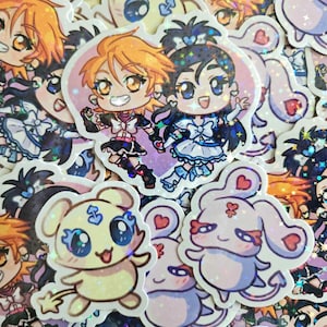 Könnte beinhalten: Eine Sammlung holografischer Aufkleber mit Anime-Charakteren. Die Aufkleber zeigen zwei Mädchen in farbenfrohen Outfits sowie niedliche tierähnliche Charaktere. Die Aufkleber haben ein glitzerndes, schillerndes Finish.