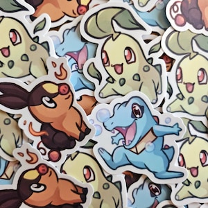 Peut inclure: Une collection d'autocollants colorés représentant diverses créatures de dessins animés. Les autocollants présentent un personnage vert clair ressemblant à un dinosaure, une créature marron et orange et un personnage bleu ressemblant à un dinosaure.