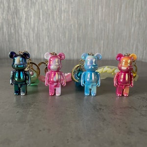 May include: Four iridescent bear keychains in different colors: teal, pink, blue, and red. Each bear has a gold ring and a gold chain attached.