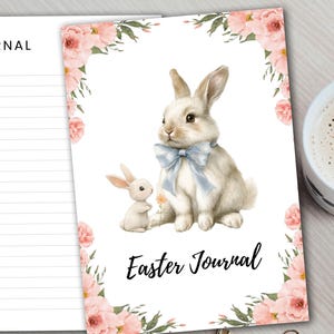 Könnte beinhalten: Oster-Journal mit einer Aquarellillustration von zwei Hasen, einer mit einer blauen Schleife. Das Cover ist mit rosa Rosen und Grünzeug verziert. Das Wort "Journal" ist auf der linken Seite gedruckt.