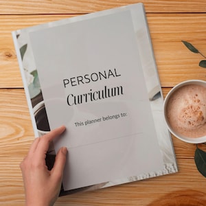 Könnte beinhalten: Ein persönlicher Lehrplaner mit dem Titel "PERSONAL Curriculum" und der Aufforderung "This planner belongs to:" ist auf einer Holzoberfläche geöffnet. Eine Tasse Kaffee und ein Zweig Blätter liegen neben dem Planer.