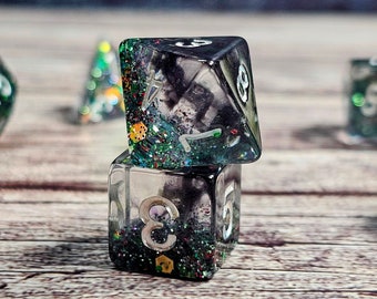May include: A set of six clear dice with black and green glitter embedded in the resin. The dice are stacked on top of each other, with the top die showing a 3 and the bottom die showing a 5.