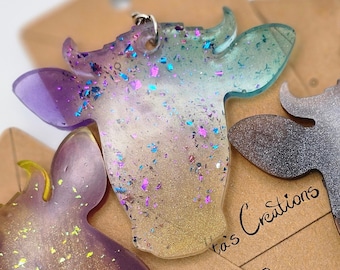 May include: Three resin cow head keychains with glitter embedded in the resin. The cow heads are in shades of purple, blue, and black. The keychains are on brown card stock with the text "Atta's Creations LLC" written on them.