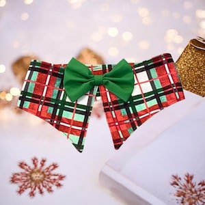 Puede incluir: Un collar para mascotas con temática navideña, con un lazo verde y un estampado a cuadros rojo, negro y blanco. El collar está diseñado para ocasiones festivas. El lazo verde proporciona un contraste llamativo con el diseño a cuadros.