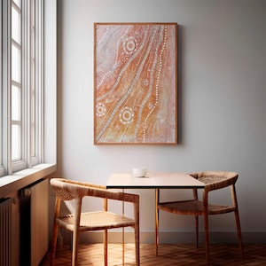 May include: A framed abstract painting with a light brown background and white dots and lines. The painting is hanging on a white wall above a table with two chairs.