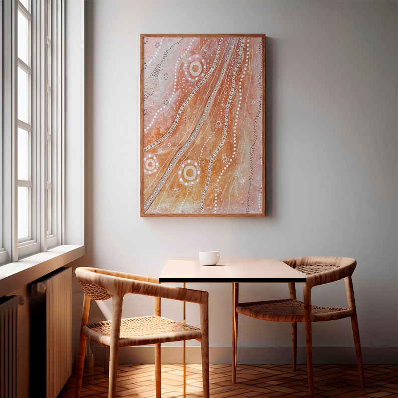 May include: A framed abstract painting with a light brown background and white dots and lines. The painting is hanging on a white wall above a table with two chairs.