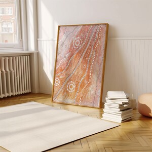 May include: A framed abstract painting with a light brown background and white and gold geometric patterns. The painting is leaning against a white wall.