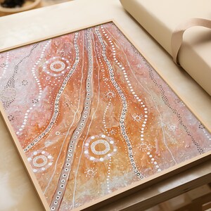 May include: A framed abstract painting with a white, brown, and orange color scheme. The painting features a series of white dots and circles on a brown and orange background.