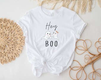 Può includere: Maglietta bianca con una grafica in bianco e nero di due fantasmi con il testo "Hey Boo" su di essa.