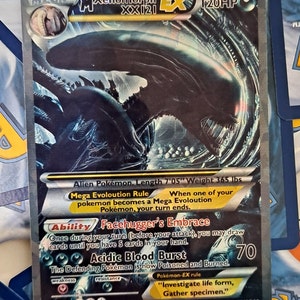 May include: A black and silver Pokemon trading card featuring a Xenomorph from the Alien franchise. The card is a Mega Evolution card with 120 HP. The card text reads "Mega Evolution Rule: When one of your pokemon becomes a Mega Evolution Pokemon, your turn ends." The card also has an ability called "Facehugger's Embrace" and an attack called "Acidic Blood Burst".