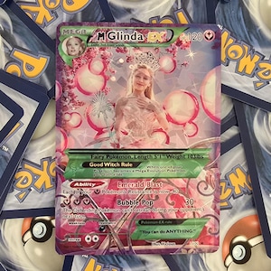 May include: A pink and purple Pokemon card featuring a woman in a white dress and a crown. The card is titled "M Glinda EX" and has a HP of 120. The card text reads "Fairy Pokemon. Length 5'1" Weight 103lbs. Good Witch Rule: When one of your Pokemon becomes a Mega Evolution Pokemon, your turn ends. Ability: Emerald Blast - Each of your Pokemon's Resistance is now -40. Bubble Pop - 30. The Defending Pokemon can't retreat during your opponent's next turn. Pokemon-EX rule: "You can do ANYTHING." Illus. Vicious 1100"