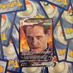 May include: A Dayman VMAX Pokemon card featuring a man with a serious expression. The card is blue, yellow, and red with the text "Dayman VMAX 330" and "Golden God" on it. The card has a Rapid Strike symbol and the text "I am untethered and my 90+ rage knows no bounds".