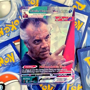May include: A trading card featuring a portrait of a man with graying hair pointing his finger. The card displays the text Paulie Walnuts VMAX, 260 HP, Bada Bing, and Homophobic Slur. The background has a holographic finish with blue and pink tones.