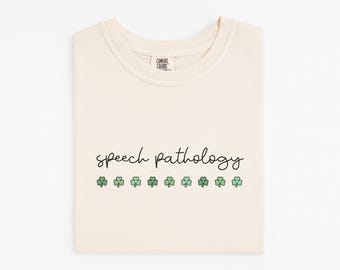 May include: Ivory t-shirt with the text "Speech Pathology" and a row of green shamrocks.