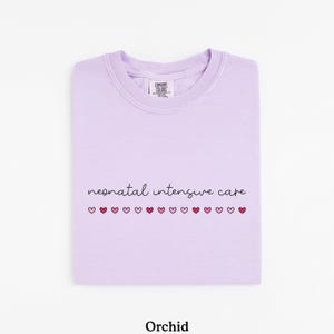 May include: A lavender colored t-shirt with the text "neonatal intensive care" and a row of small pink and red hearts.