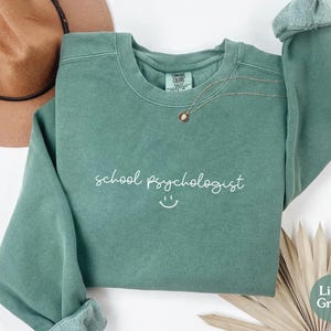 May include: Light green sweatshirt with the text "school psychologist" and a smiley face in white.