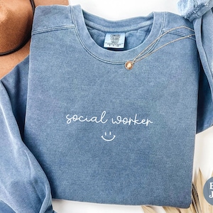 May include: A blue jean sweatshirt with the text "social worker" and a smiley face embroidered in white.