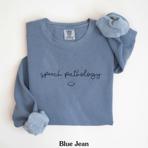May include: A blue jean sweatshirt with the text "speech pathology" and a smiley face printed on the front.
