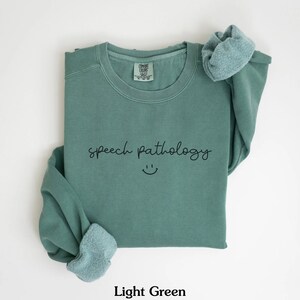 May include: Light green sweatshirt with the text "speech pathology" and a smiley face.