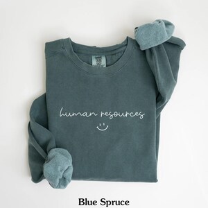 May include: A teal blue sweatshirt with the text "human resources" and a smiley face in white.