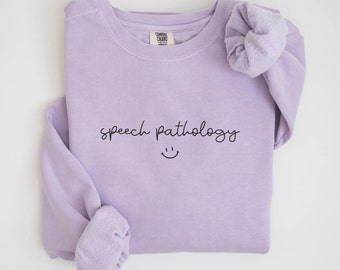 May include: A light purple sweatshirt with the text "speech pathology" and a smiley face in black.