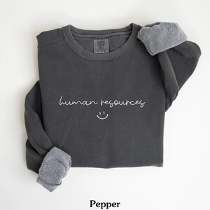 May include: A dark gray sweatshirt with the text "human resources" and a smiley face in white.