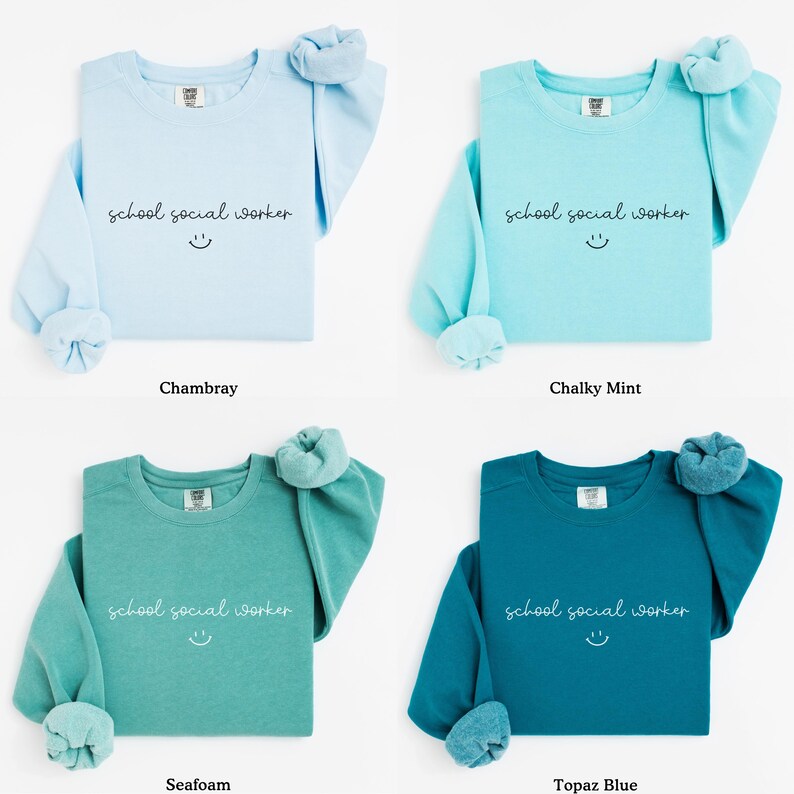 Puede incluir: Cuatro sudaderas con cuello redondo en diferentes colores: Chambray, menta calc&aacute;rea, espuma de mar y azul topacio. Cada sudadera tiene el texto "school social worker" y una carita sonriente impresa en la parte delantera.