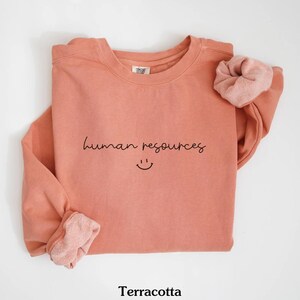 May include: Terracotta colored sweatshirt with the text "human resources" and a smiley face in black.
