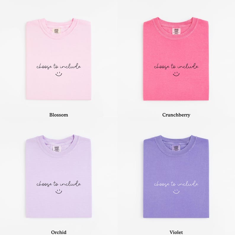 May include: Four folded t-shirts in different colors: blossom, crunchberry, orchid, and violet. Each shirt has the phrase "choose to include" and a smiling face printed on the front.