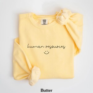 May include: A yellow sweatshirt with the text "human resources" and a smiley face in black.