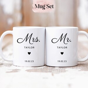 May include: A set of two white ceramic mugs with black lettering. The mugs say "Mrs. TAYLOR" and "Mr. TAYLOR" with a heart and the date "19.02.23" on each mug.
