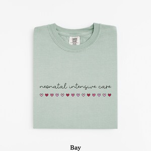 May include: A light green t-shirt with the text "neonatal intensive care" and a row of pink and red hearts.