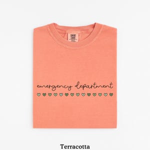 May include: Terracotta colored t-shirt with the text "emergency department" and a row of green hearts.