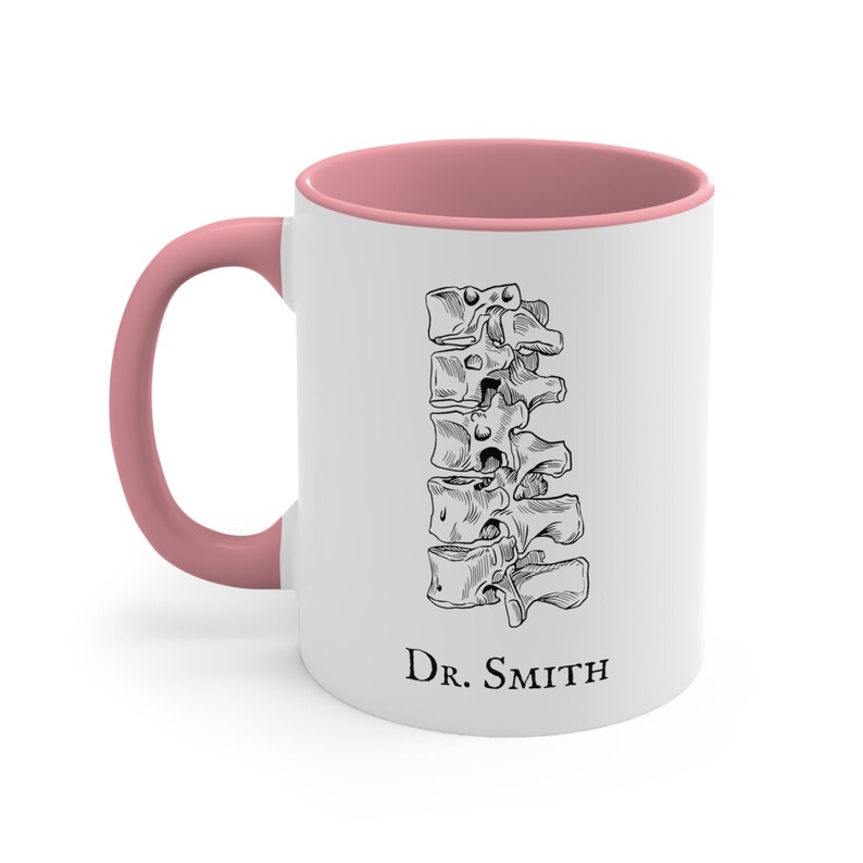 May include: White ceramic mug with a pink rim and handle. The mug features a black and white illustration of a human spine and the text "Dr. Smith" at the bottom.