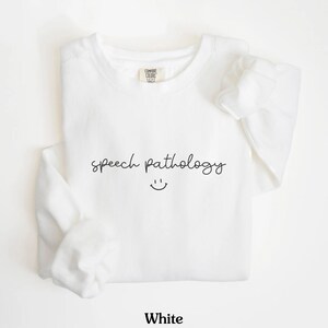 May include: White sweatshirt with the text "speech pathology" and a smiley face.