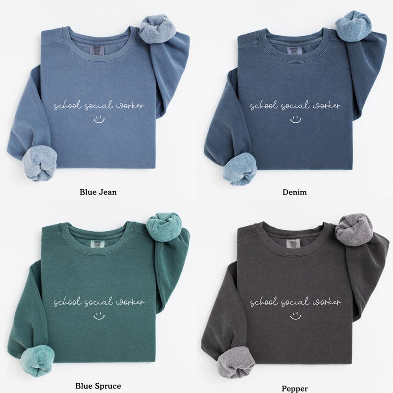 Puede incluir: Cuatro sudaderas con cuello redondo en diferentes colores: azul vaquero, denim, azul abeto y pimienta. Cada sudadera tiene el texto "school social worker" y una carita sonriente impresa en la parte delantera.
