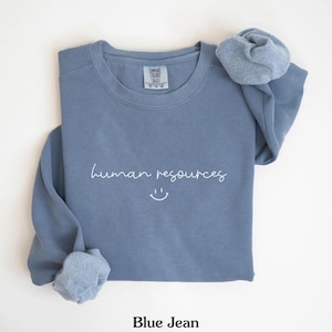 May include: A blue sweatshirt with the text "human resources" and a smiley face in white.