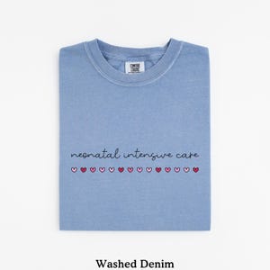 May include: A light blue t-shirt with the text "neonatal intensive care" and a row of pink and red hearts. The shirt is made of a washed denim fabric.