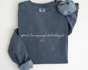 May include: A dark blue sweatshirt with the text "speech language pathologist" and a smiley face in white.