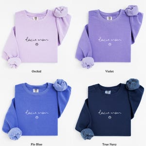 May include: Four crewneck sweatshirts in orchid, violet, flo blue, and true navy. Each sweatshirt has the text "doxie mom" with a paw print graphic. The sleeves are cuffed, and the colors are solid.