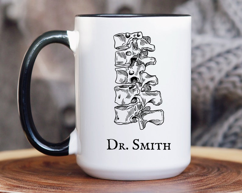 May include: White ceramic mug with a black handle. The mug features a black and white illustration of a human spine and the text "Dr. Smith".