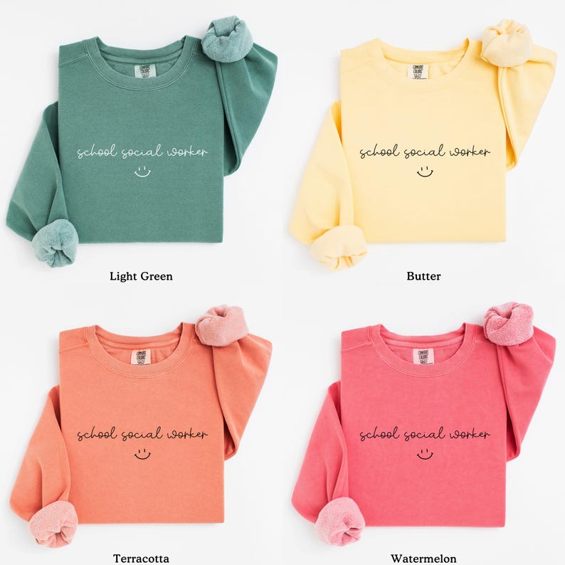 Puede incluir: Cuatro sudaderas de manga larga en diferentes colores: verde claro, amarillo, naranja y rosa. Cada sudadera tiene el texto "school social worker" con una carita sonriente impresa en la parte delantera.