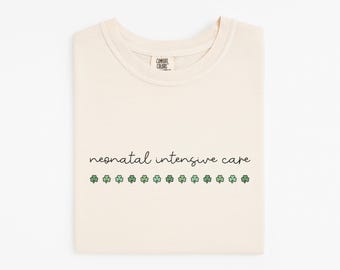 May include: Ivory t-shirt with the text "neonatal intensive care" and a row of green shamrocks.