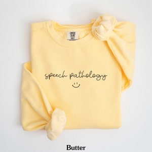 May include: A yellow sweatshirt with the text "speech pathology" and a smiley face in black.