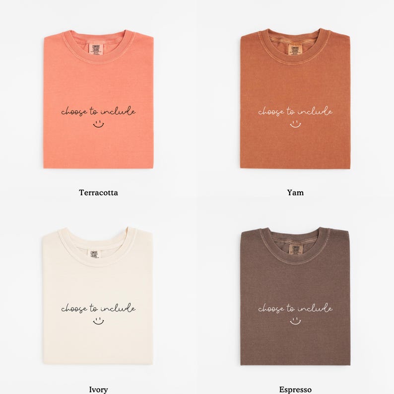 May include: Four folded t-shirts in terracotta, yam, ivory, and espresso colors. Each shirt has the phrase "choose to include" and a smiling face printed on the front. The shirts are displayed on a white background.