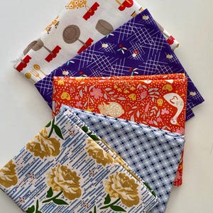 Peut inclure: Une pile de cinq carrés de tissu pliés présentant des motifs variés : un tissu blanc avec des ustensiles de cuisine, un imprimé à grille violet, un tissu orange à motifs floraux et animaliers, un motif géométrique bleu clair et un imprimé floral à rayures bleues.