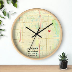 May include: A round wooden clock with a map of a city printed on the face. A red heart marks a spot on the map. The text "Where we met Ana & Patrick 26°2'10.38"N 80°8'36.99"W" is printed below the map.