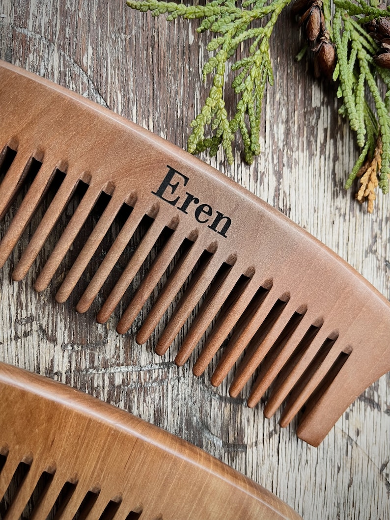 May include: A wooden comb with a curved handle and the name "Eren" engraved on the top. The comb is brown and has a natural wood finish.