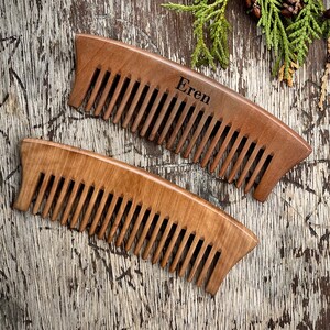 May include: Two wooden combs, one with the name "Eren" engraved on it, on a rustic wooden background.