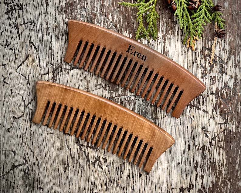 May include: Two wooden combs, one with the name "Eren" engraved on it, on a rustic wooden background.
